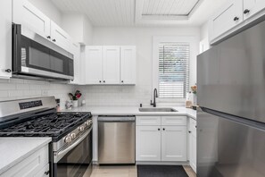 A modern kitchen with white cabinetry, stainless steel appliances, and a black countertop. - Sandy Shores • Steps to Beach & Frenchy's • Pet Friendly • Patio ➠ 20 Kendall 1 (Clearwater)