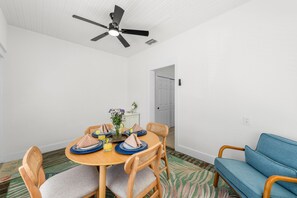 A dining area with a round table, chairs, a ceiling fan, and a blue sofa. - Sandy Shores • Steps to Beach & Frenchy's • Pet Friendly • Patio ➠ 20 Kendall 1 (Clearwater)