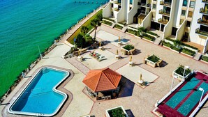 Eine Vogelperspektive zeigt ein Resort mit zwei Schwimmbecken, einer überdachten Sitzgelegenheit und einer Strandpromenade.
