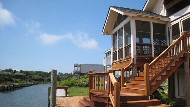 A waterfront property with a wooden deck, a covered outdoor area with stairs, and a view of the water.