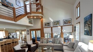 A spacious living area with a high ceiling, a wooden staircase, and a kitchen area.