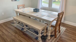 A dining area with a wooden table and bench, a chandelier, and a view of the outdoors. - Pelican's Perch: Centrally located Dog friendly condo with pool. (Ocracoke)
