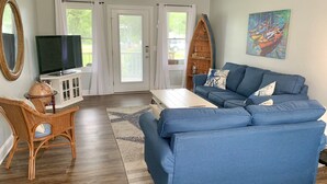 A living room with a blue sofa, a television, a globe, and a wooden boat shelf. - Pelican's Perch: Centrally located Dog friendly condo with pool. (Ocracoke)