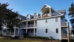 A two-story house with a covered porch, a second-floor balcony, and a small front yard. - Pelican's Perch: Centrally located Dog friendly condo with pool. (Ocracoke)
