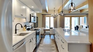Een moderne keuken met witte kasten, een centraal eiland en een eetgedeelte met een kroonluchter.