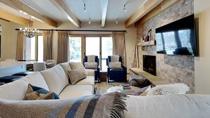 Een ruime woonkamer met een grote bank, fauteuils, een open haard en een televisie die aan een stenen muur is bevestigd.