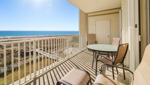 Ein Balkon mit Tisch und Stühlen und Blick auf den Strand, sowie eine Tür.