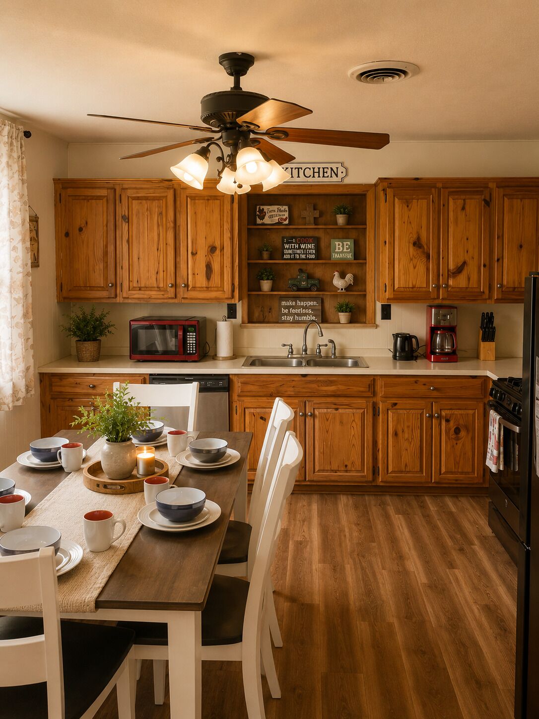 A kitchen with wooden cabinets, a dining table with chairs, a ceiling fan, and a sign that reads 'KITCHEN'.