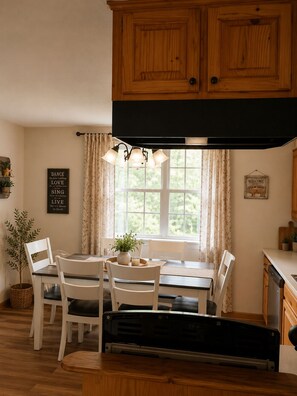Una cocina con armarios de madera, una mesa de comedor con sillas, un banco y una ventana con cortinas.