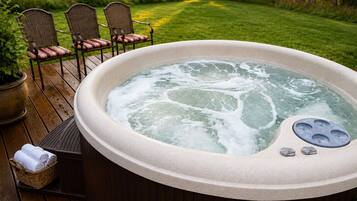 A hot tub on a wooden deck with chairs and a basket of towels.