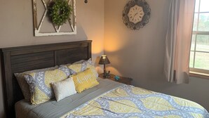 Een slaapkamer met een bed, een wandklok, een hanglamp en een raam met gordijnen.