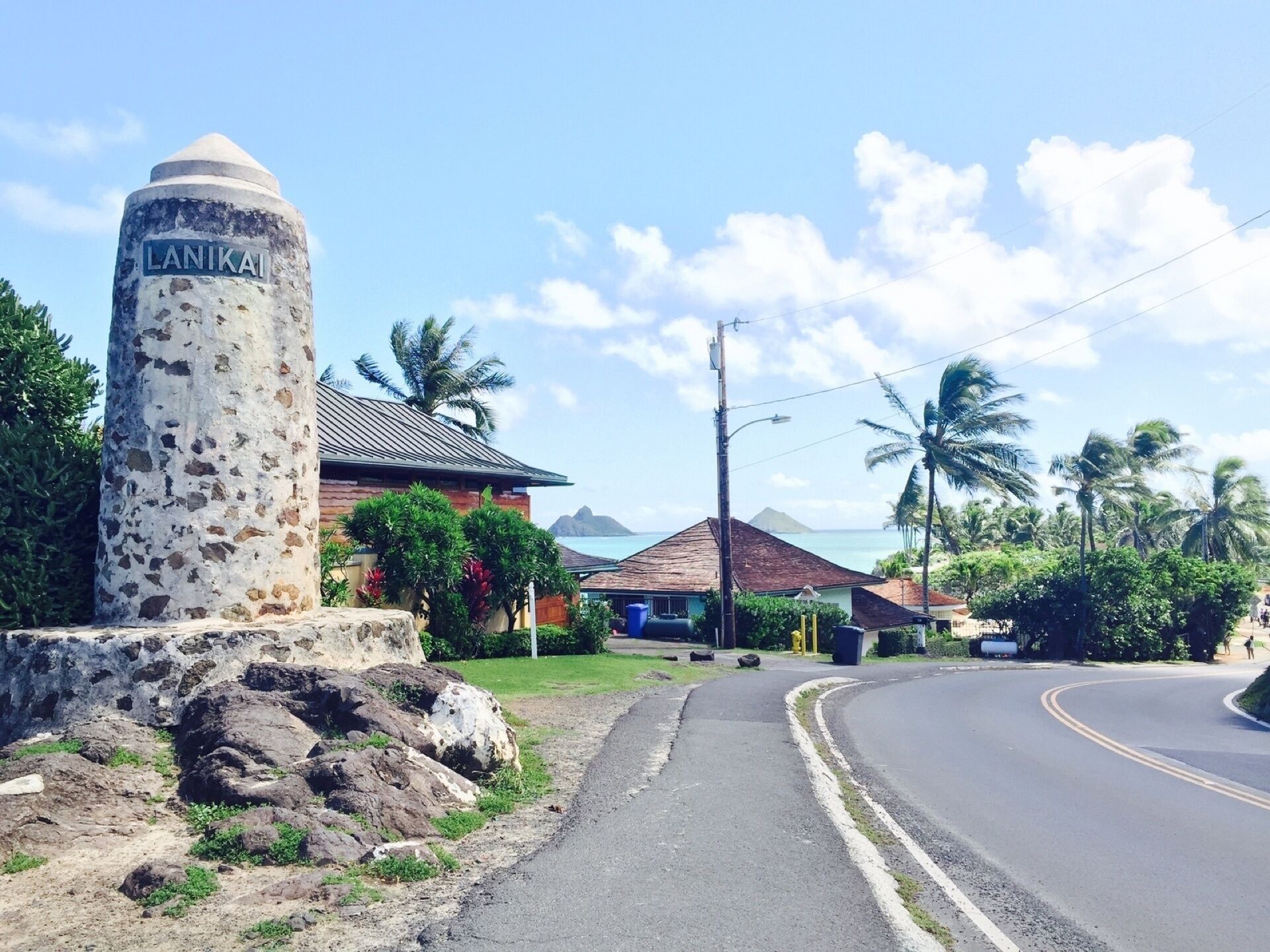 A coastal road with a stone monument labeled "LANIKAI" and a building with a red roof.