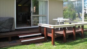Un espacio al aire libre cubierto con una mesa, sillas, una parrilla y una puerta corrediza de vidrio que da a un espacio interior.