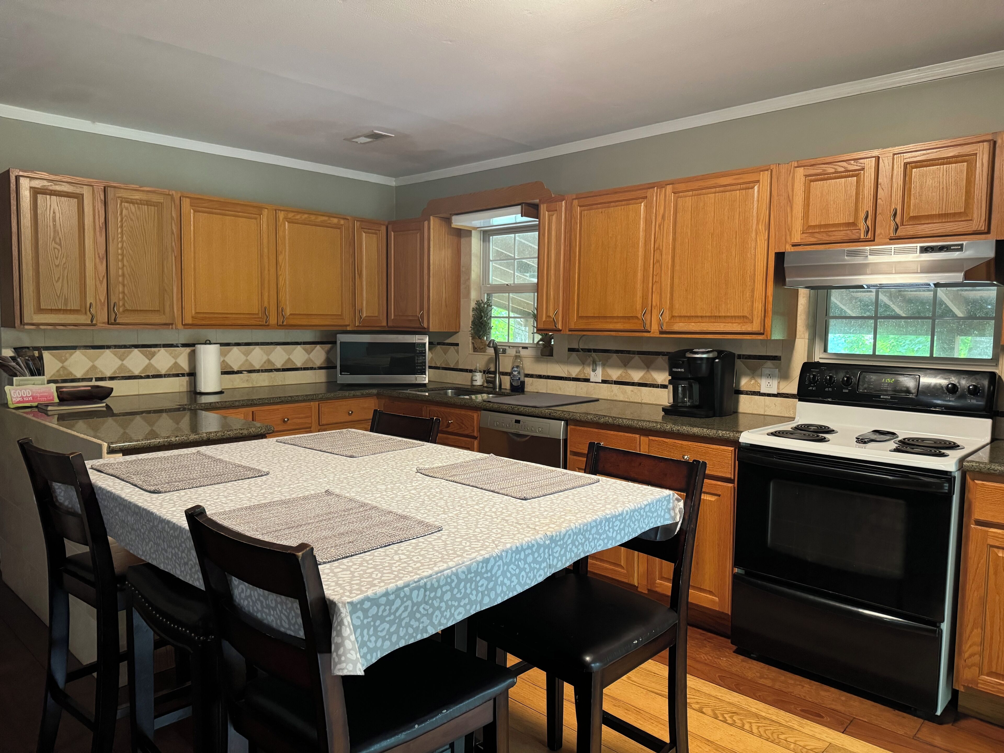 A kitchen with wooden cabinets, a microwave, a coffee maker, a stove, and a dining table with chairs.