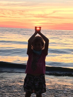 Una persona forma un corazón con las manos contra un fondo de atardecer.