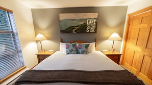 Een slaapkamer met een groot bed, twee nachtkastjes met lampen, een houten garderobe en een schilderij van een meer aan de muur.