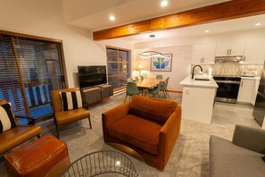 A modern living room with a sofa, a TV, and a dining area with chairs and a table. - Forest Trails - Easy Ski Access, Private Garage, Free Village Shuttle (Whistler)