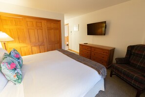 Een slaapkamer met een bed, een houten garderobe, een dressoir, een televisie en een geruit fauteuil.