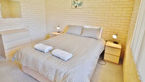 Ein Schlafzimmer mit Backsteinwand, einem Bett mit gemustertem Überwurf, zwei Nachttischen mit Lampen, einer Kommode und einem gerahmten Kunstwerk an der Wand.