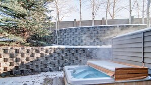 A hot tub in a backyard with a stone wall and wooden deck. - River Ridge Townhomes - Sleek Family Foxhole Retreat with Private Hot Tub (Ketchum)