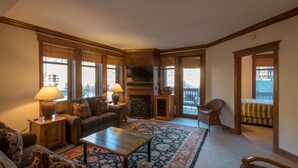 A cozy living room with a fireplace, a sofa, a coffee table, and a view of the city through large windows.