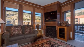 A living room with a sofa, TV, fireplace, and large windows with a view of the outdoors.