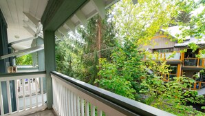 Ein Balkon mit weißer Brüstung, der auf einen üppigen Garten und ein Gebäude mit gelber Fassade blickt.