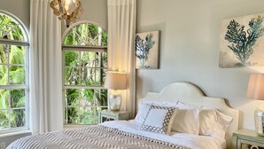 A bedroom with a large bed, two bedside tables, a chandelier, and artwork on the walls. - Exquisite Home in Exclusive Community (Naples)