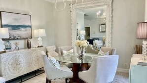 A dining room with a round glass table surrounded by six upholstered chairs, a large mirror, and a chandelier. - Exquisite Home in Exclusive Community (Naples)