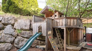 Une cabane en bois, dotée d’un toboggan et d’un mur d’escalade, entourée de rochers et d’arbres.