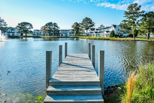 A wooden dock leading to a lake with houses in the background.