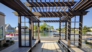 Un espacio de estar al aire libre con techado, bancos, vistas a un lago y barcos amarrados cerca.
