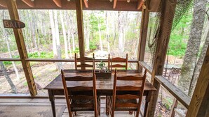 A wooden dining table with four chairs, set in a rustic wooden structure with a view of a forested area. - Creekside Serenade: Todd Cabin w/Hot Tub, Creekfront, 2 Kings & Fenced Yard (Todd)