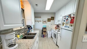 A kitchen with white cabinets, a granite countertop, a coffee maker, a sink, a stove, and a refrigerator.