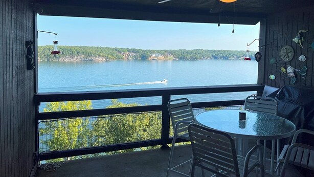 A room with a large window overlooking a lake, a round table with chairs, and a ceiling fan. - Knolls 1422 - Two Bedroom Apartment, Sleeps 6 (Osage Beach)