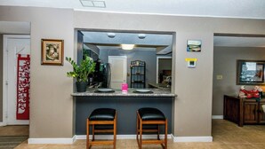 A kitchen with a large mirror, two bar stools, a potted plant, and a red decorative piece on the wall. - Knolls 1422 - Two Bedroom Apartment, Sleeps 6 (Osage Beach)