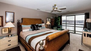 A hotel room with a bed, bedside lamps, a television, a desk, a chair, a window with a view, and a ceiling fan. - Knolls 1422 - Two Bedroom Apartment, Sleeps 6 (Osage Beach)