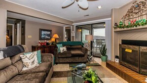 A living room with a ceiling fan, a fireplace, a glass coffee table, and a view through a glass door. - Knolls 1422 - Two Bedroom Apartment, Sleeps 6 (Osage Beach)