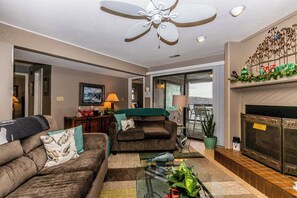A living room with a ceiling fan, a fireplace, a glass coffee table, and a view through a glass door. - Knolls 1422 - Two Bedroom Apartment, Sleeps 6 (Osage Beach)