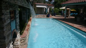 A swimming pool with a stone wall on one side and a covered area with chairs and umbrellas on the other. - Three bedroom/three bath resort style home with saltwater pool and spa  (Three Rivers)