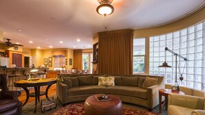 A spacious living room with a curved sofa, a coffee table, and a large window with curtains. - Three bedroom/three bath resort style home with saltwater pool and spa  (Three Rivers)