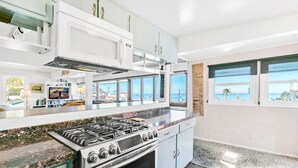 Une cuisine moderne équipée d’une cuisinière à gaz, d’un four à micro-ondes et de grandes fenêtres offrant une vue sur la mer.