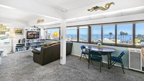 Un salon spacieux doté d’une grande fenêtre donnant sur une plage, d’un canapé confortable, d’une table à manger avec des chaises et d’une bibliothèque remplie de livres.