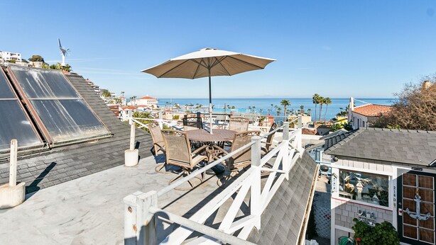 Une terrasse sur le toit, avec une table et des chaises, un grand parasol et une vue sur l’océan.