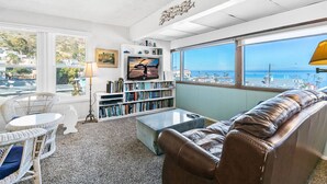 Un salon avec un canapé en cuir, une table basse, une bibliothèque et une vue sur l’océan.