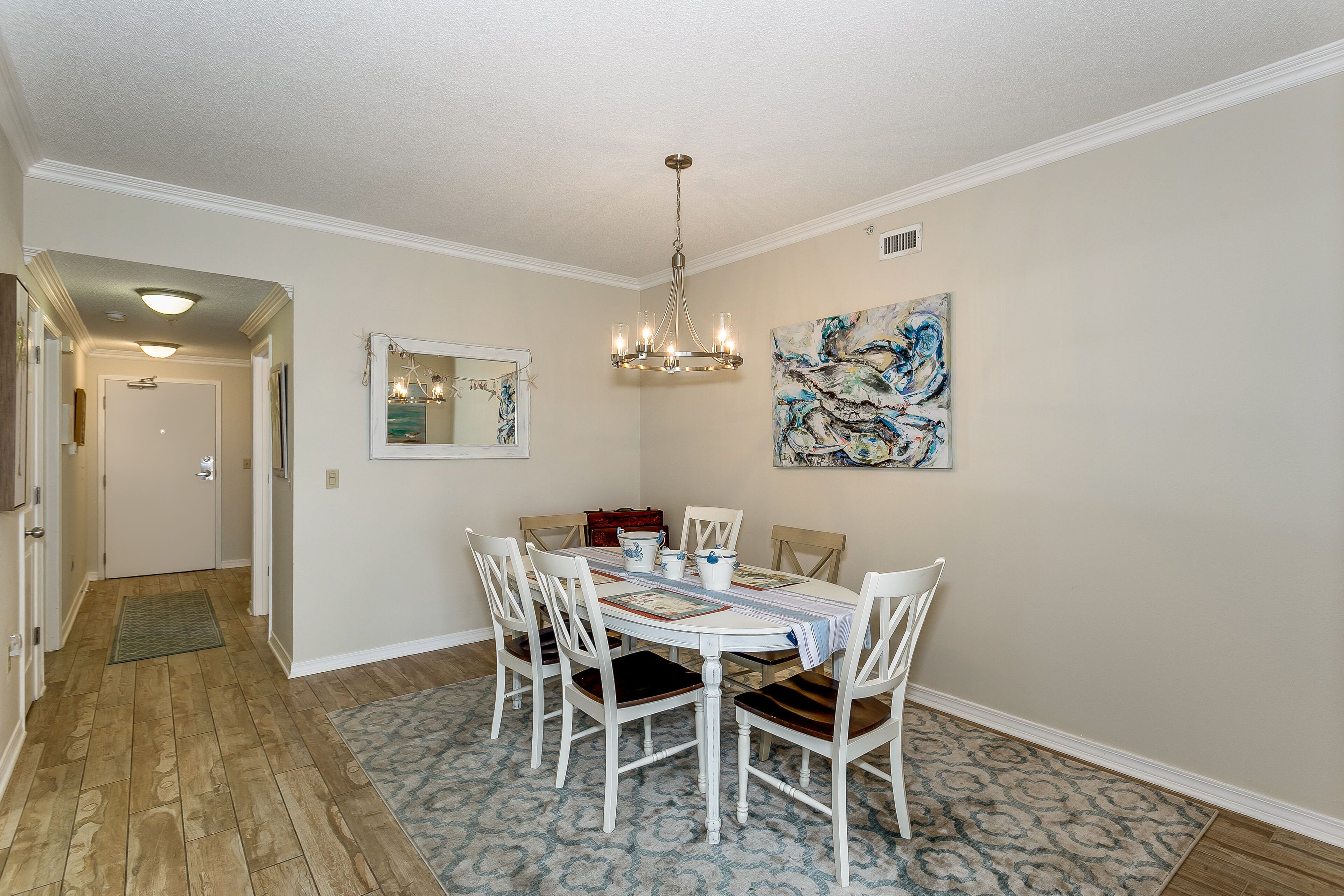 A dining room with a chandelier, a table set for four, and a painting on the wall.