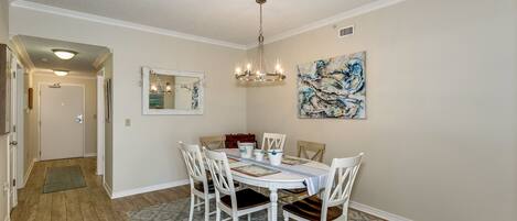 A dining room with a chandelier, a table set for four, and a painting on the wall.