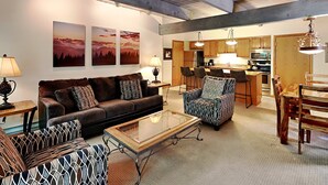 A spacious living area with a sofa, armchair, and coffee table, a kitchen with wooden cabinets, and a dining table with chairs. - 🌲Timberline A2H Deluxe 2-Bedroom ~Hot Tub~Pool~WiFi~Ski-in/out~Local Shuttle🌲 (Snowmass Village)