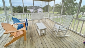 A covered porch with wooden flooring, white rocking chairs, and a table.