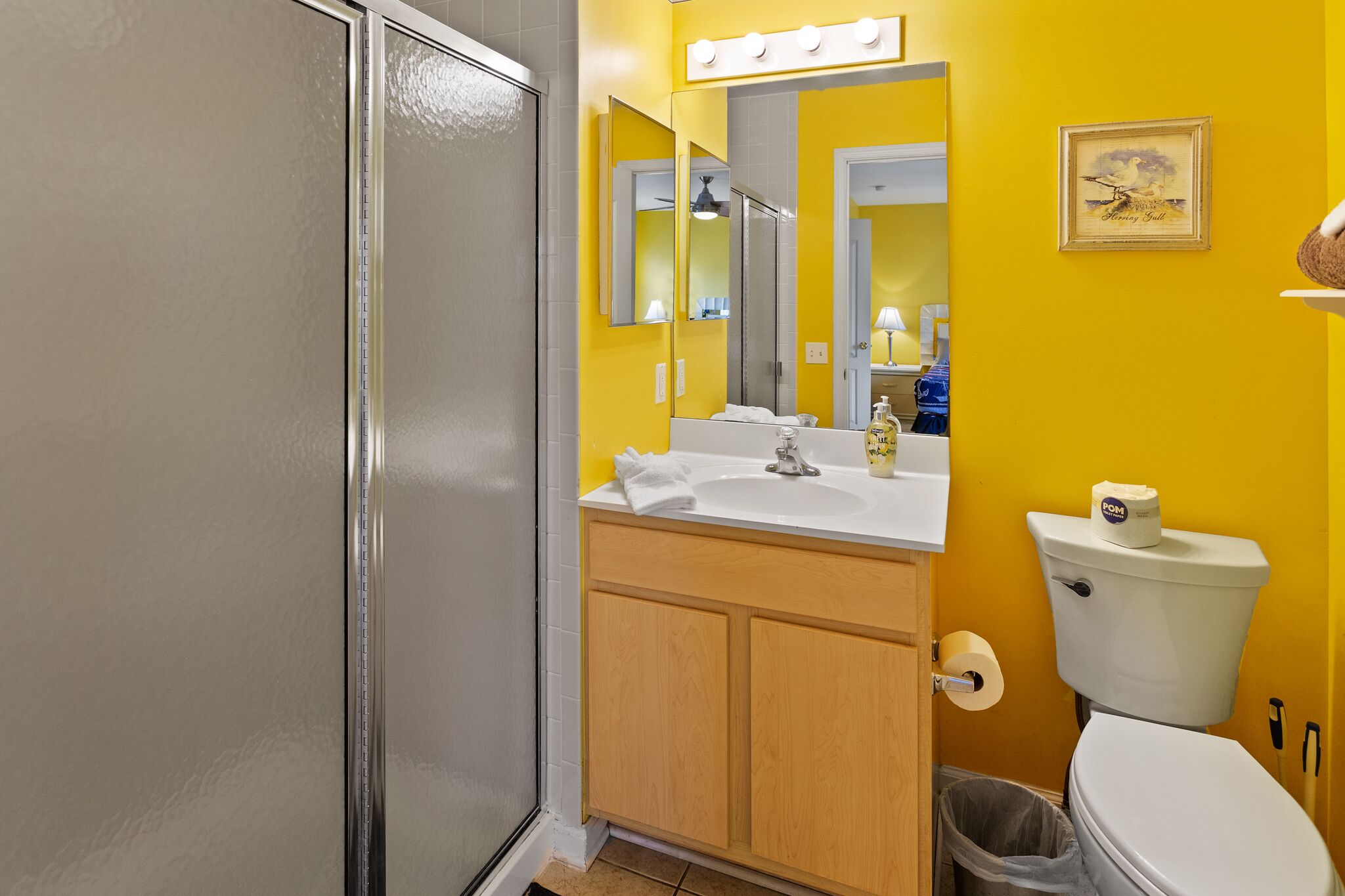 Un baño con inodoro blanco, lavamanos con espejo y zona de ducha.